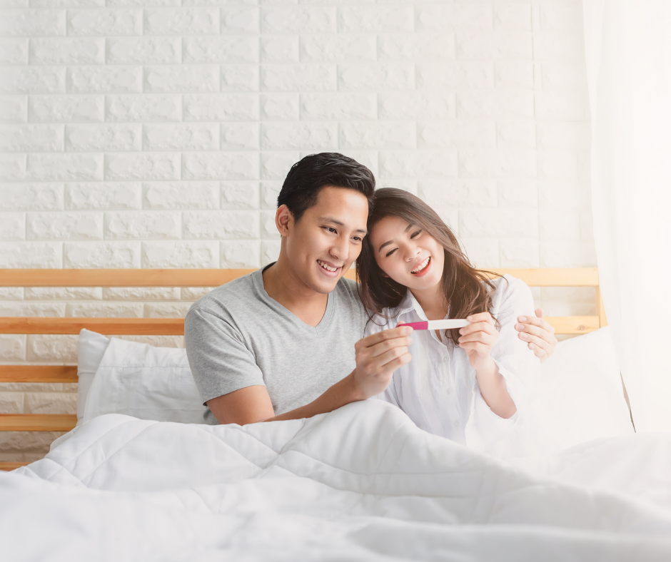 couple in bed looking at pregnancy test